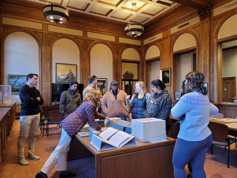 eight people crowd around a table of archival materials