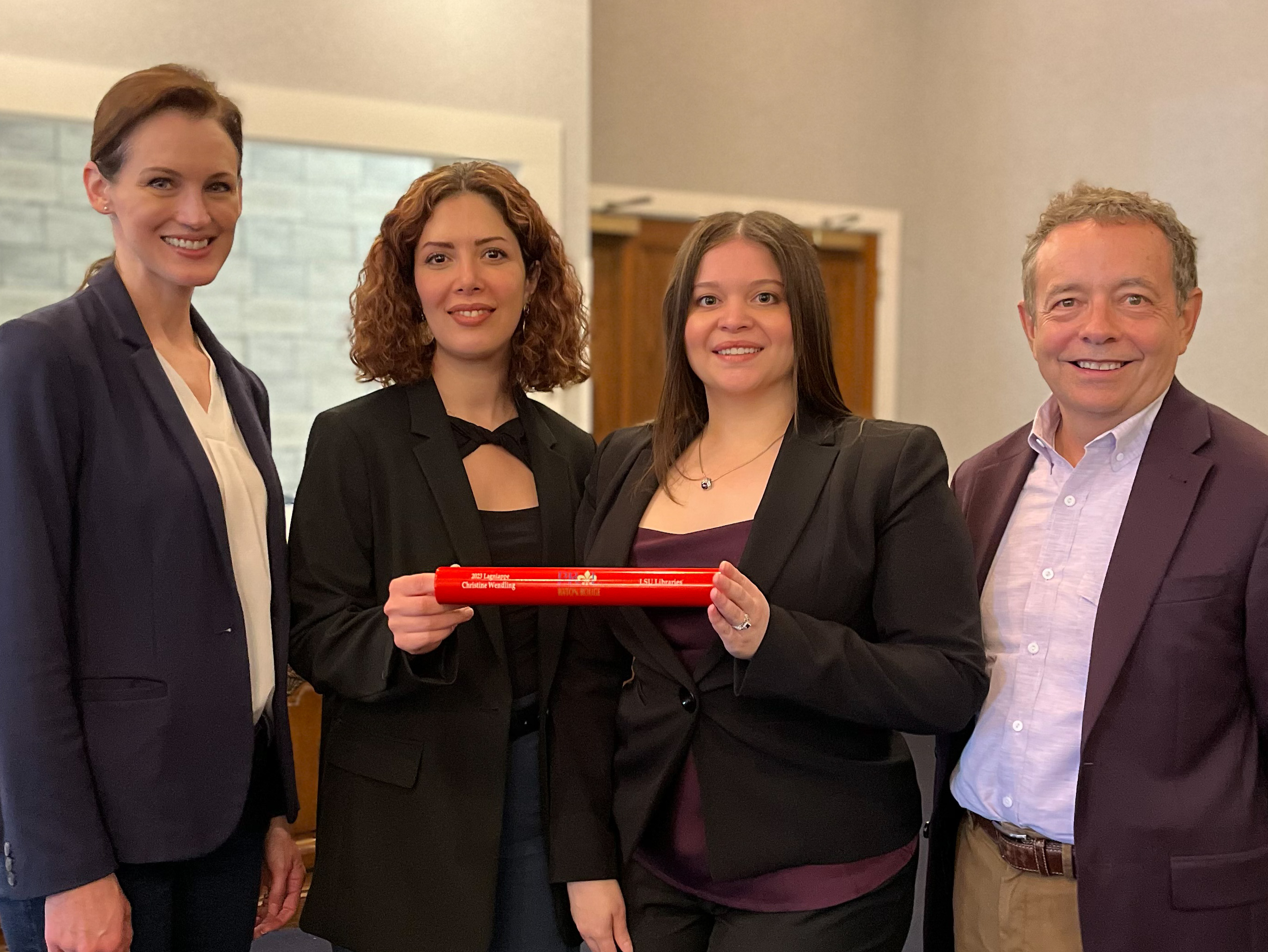 three women and a man pose with a red stick award