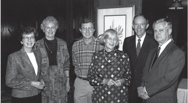 black and white picture of five people of mixed genders in front of a framed photo of a plant
