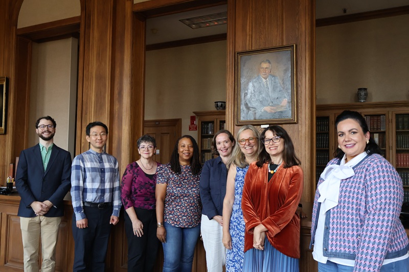 Eight people stand together and smile indoors
