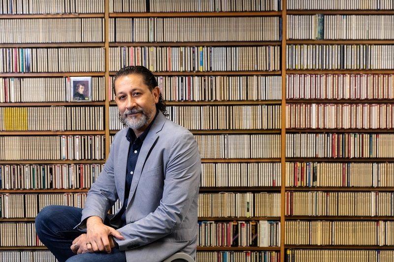 Mikel LeDee sits in front of shelves of musical scores