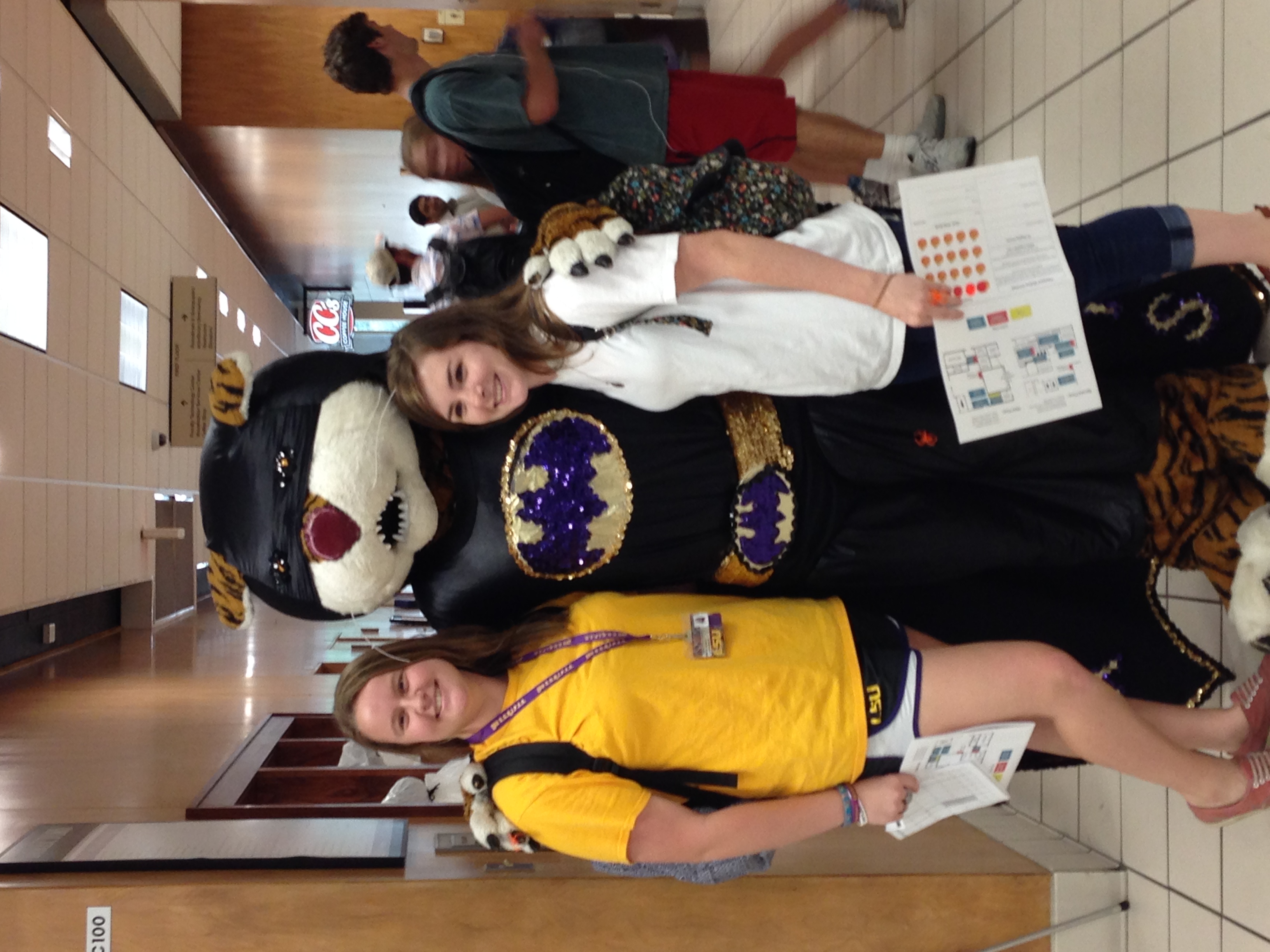 two women pose with Mike the Tiger dressed as Batman in the LSU library