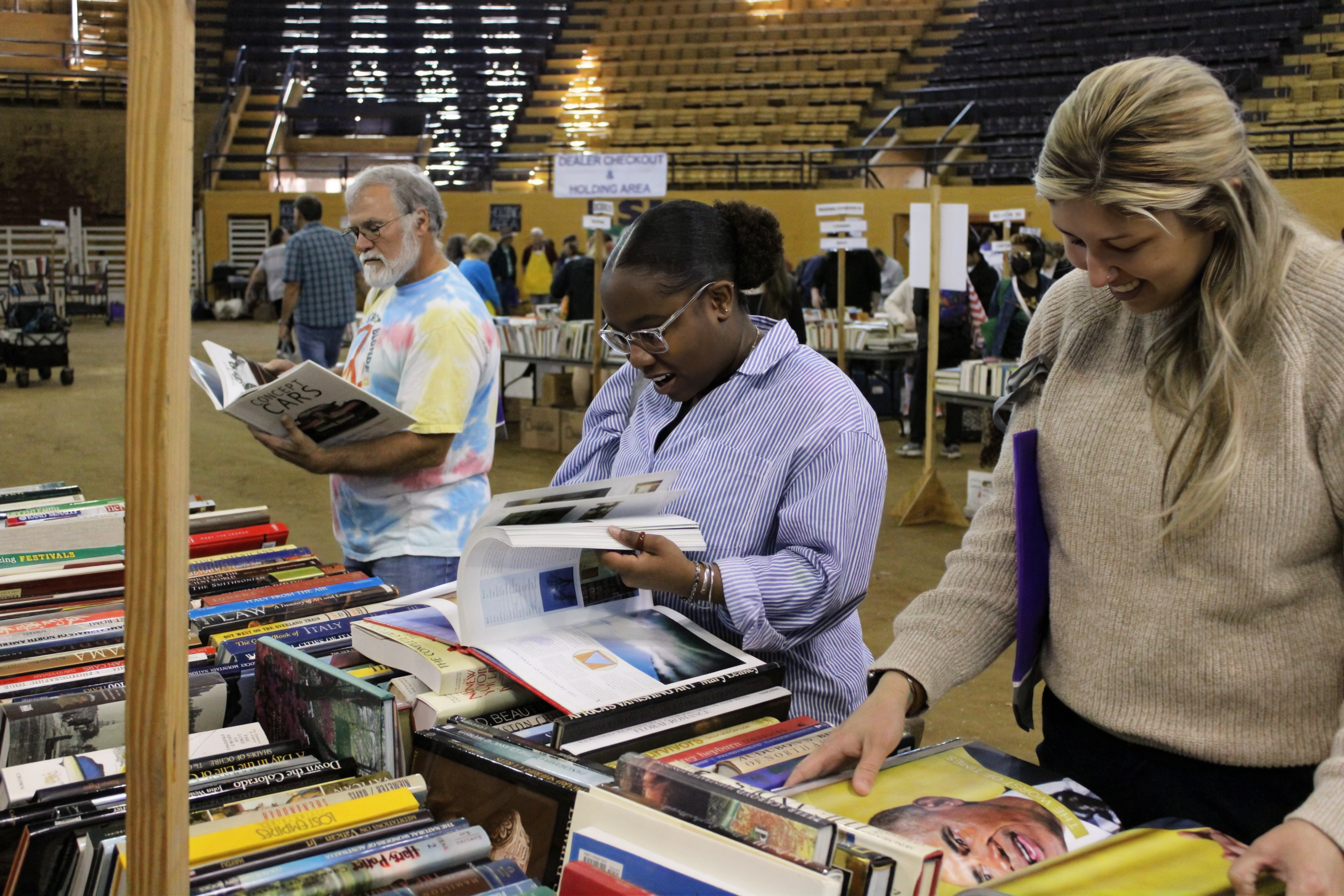 three people page through books next to a long table filled with even more titles