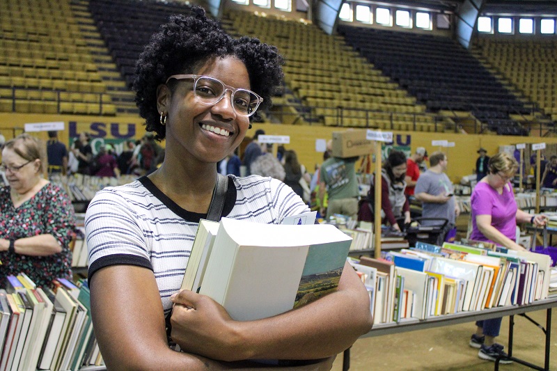 a woman smiles while clutching a stack of books to her chest