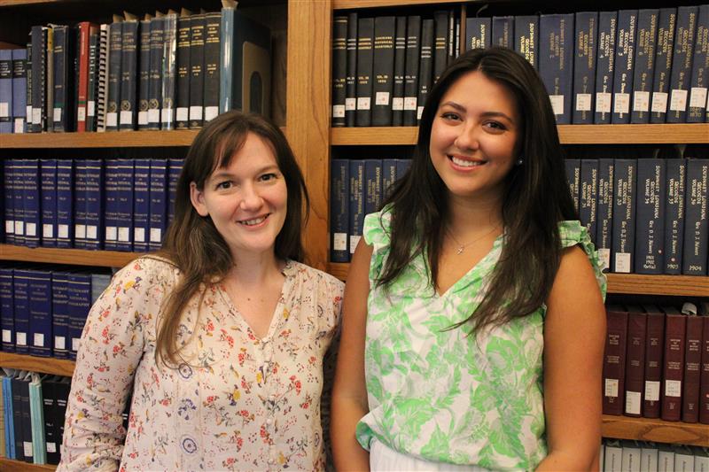 two women smile in front of a large bookcase